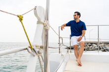 Caucasian Man Passenger Tourist Resting On Luxury Private Catamaran Boat Yacht Sailing In The Ocean At Summer Sunset. Handsome Guy Enjoy Outdoor Lifestyle Travel Tropical Island On Holiday Vacation.