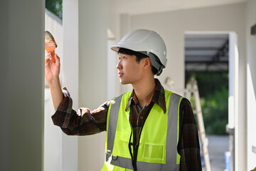 Asian male painter in safety helmet holding painting brush painting a white wall. Home renovation concept