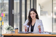 © David - Asian Businesswoman having a tea, sitting on desk in workplace, writing down notes, opened laptop in document the financial report, business plan investment, finance analysis concept.