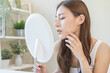 © KMPZZZ - Dermatology, puberty asian young woman, girl looking into mirror, allergy when wear mask and cosmetic, show squeezing pimple spot for removing from face.Beauty care from skin problem by acne treatment