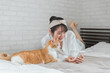 © buritora - 家のベッドルームでペットの猫とスマホで写真を撮って遊ぶアジア人女性