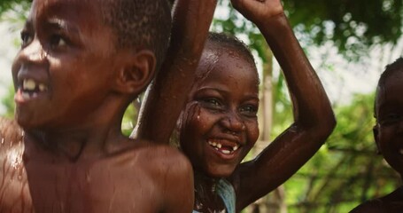 Wall Mural - Portrait of an African Little Girl Jumping and Dancing with Other Kids Under Pouring Water. Happy and Innocent Black Children Playing and Enjoying the Blessing of Rain Water After Long Drought