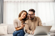 © dusanpetkovic1 - Happy couple is sitting in a living room and shopping online on a laptop at home.