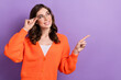 Photo of nice smile pretty lady brunette curly hair touch glasses wear orange cardigan direct finger empty space isolated on violet color background