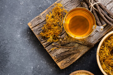 Wall Mural - Glass cup of licorice tea with licorice root and fiber on rustic background, alternative medicine ( glycyrrhiza glabra )