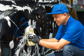 Wall Mural - Man worker washing car service with foam and sponge. Car wash cleaning wipe station. Employees clean a vehicle professionally.