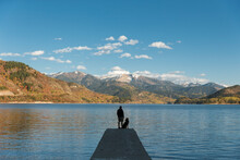 Silhouette Of Man Standing On Lake Jetty With German Shepherd And Admiring Beautiful Landscape, Swan Valley, Idaho, USA