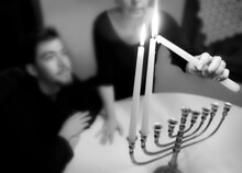 A Jewish Family Celebrates Hanukkah At Home By Lighting The Candles Of A Menorah.