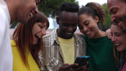 Wall Mural - Young happy student friends having fun together using mobile phone standing outdoors. Multi-ethnic group of millennial people laughing while watching funny social media content on smartphone app.