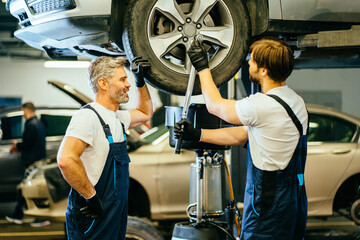 Wall Mural - Mature and young adult mechanics, father and son working together in large modern car repair service. Family business concept.