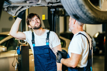 Wall Mural - Two mechanics in uniform father and son are working in auto service with lifted vehicle.