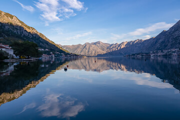  Panoramic view of bay of Kotor at sunrise in summer, Adriatic Mediterranean Sea, Montenegro, Balkans, Europe. Fjord winding along coastal towns. First sunbeams on Lovcen mountains. Water reflection