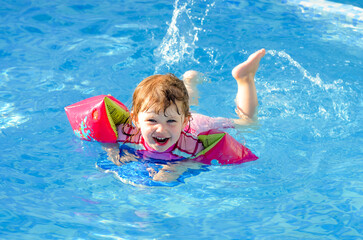 Wall Mural - Beautiful young girl playing in the pool with her arm bands