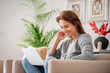 © sepy - Smiling caucasian woman using laptop while sitting in an armchair at home