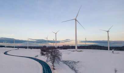 Wall Mural - aerial view of wind turbines on the snow covered field at sunset