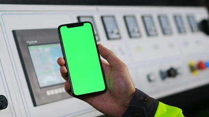 Close up of black smartphone with green screen in Caucasian male hand of workman at plan. Controlling point at factory. Plant control with device app on mobile phone. Green screen concept.