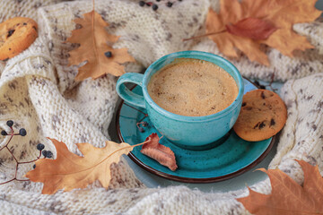 Wall Mural - Autumnal composition with white knitted scarf, blue cup of coffee, cookies and dry yellow leaves on a table. Autumn mood.