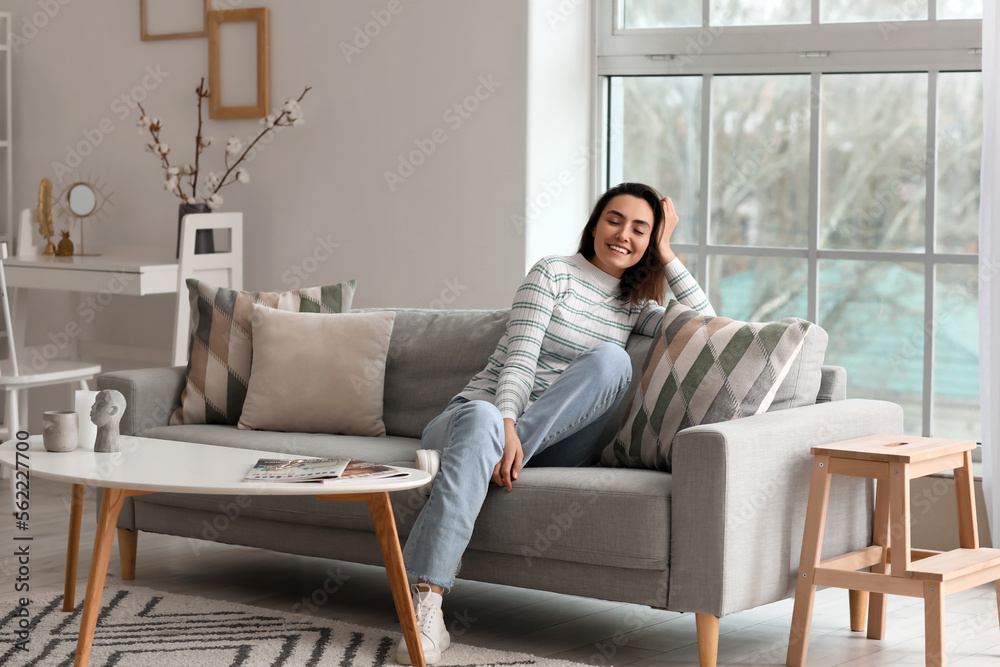Young woman sitting on grey couch in living room