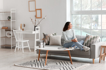 Poster - Young woman sitting on grey couch in living room