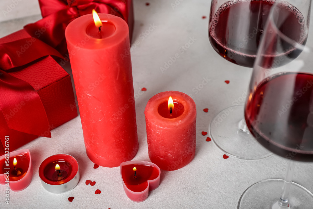 Burning candles, glasses of wine and gift boxes on light background. Valentine's Day celebration