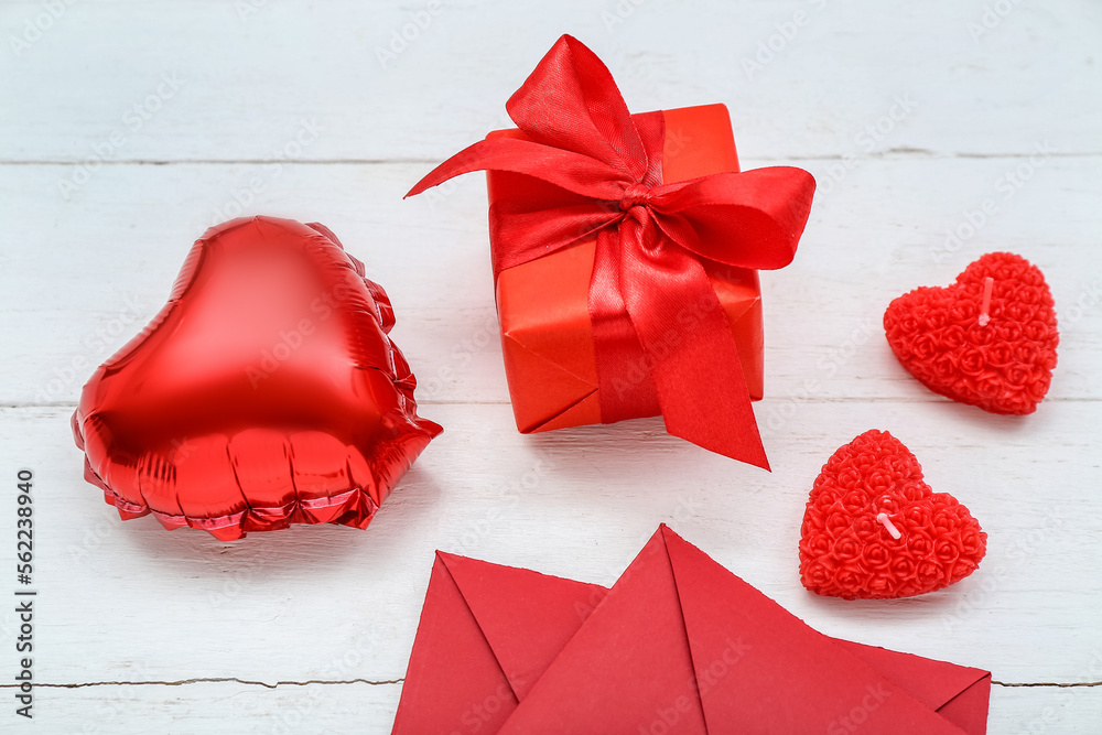 Beautiful candles, gift box and envelopes on light wooden background. Valentine's Day celebration