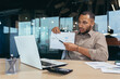 © Liubomir - Dissatisfied businessman shows a graph with bad achievements to the camera on a video call, a Latin American man reports negative results at an online meeting of company managers, a man at work.