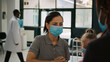 © DC Studio - Woman and little girl with facemask talking to receptionist at hospital reception counter, asking about medical appointment form. People waiting to attend consultation during covid 19 pandemic.