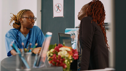 Wall Mural - Team of medical staff talking at hospital reception counter, discussing about checkup appointments with patients. Nurse and receptionist standing at facility front desk, waiting room.