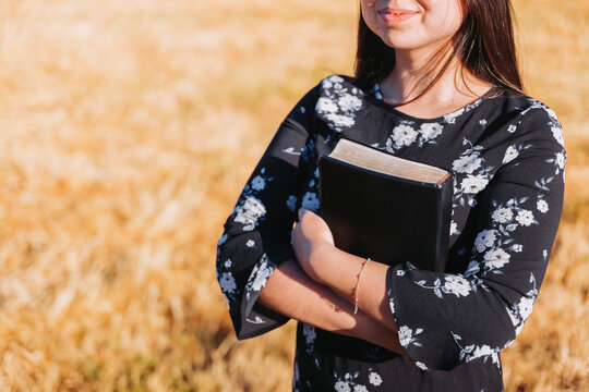 Unrecognizable christian young woman holding her bible under her arm in the field. Sola scriptura. Copy space