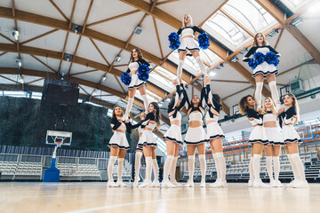 Wall Mural - Low angle shot. Three groups of cheerleaders holding their teammates in the air. Extension stunt. Sport concept. High quality photo