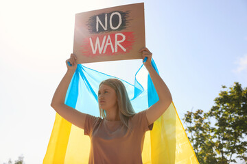 Wall Mural - Sad woman holding poster with words No War and Ukrainian flag outdoors