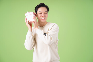 Wall Mural - Image of young Asian man holding giftbox on background