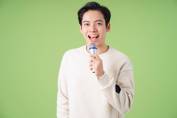 Image of young Asian man holding microphone on background