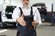 © H_Ko - Closeup of auto mechanic greeting someone and offering handshake working in auto repair shop