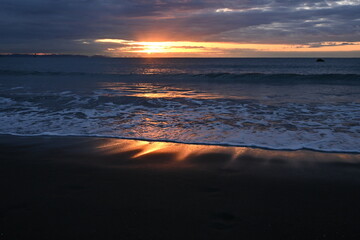 Poster - The beach at dawn when the sun's rays dye the waves red. Japanese natural background material.