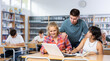© JackF - Smiling boy helping positive pupils research, working with laptop in school library