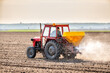 A farmer in an agricultural tractor at a farm fertilizing an arable field, a crucial step in crop production
