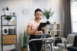 © Sofiia Shunkina - Attractive young sports african businesswoman in headset working with tablet while working out, running, doing cardio training on treadmill indoor at home.