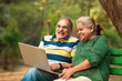 © Niks Ads - Happy senior couple sitting on bench in the park and using laptop.