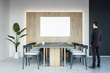 Aufkleber - Businessman back view looking at blank white poster on wooden wall decoration background in sunlit spacious meeting room with dark conference table on concrete floor, mockup