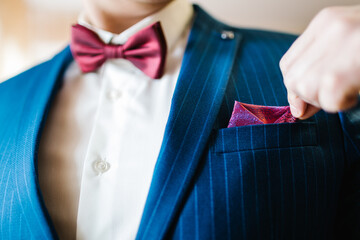 The man corrects handkerchief on the suit. The groom in a suit, shirt with bow-tie. Close up. Expensive suit, bow tie and elegant handkerchief.