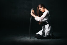 Ninja Samurai Woman Kneeling And Sitting On The Floor, Holding Katana Sword. The Concept Of Loyalty And Fidelity. Background With Copy Space.