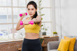 © khwanchai - Sporty young woman raises dumbbell, young Asian female exercising with her weights in the living room