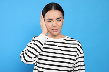 Poster - Young woman suffering from ear pain on light blue background