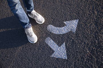 Wall Mural - Choice of way. Man standing in front of drawn marks on road, closeup. White arrows pointing in different directions
