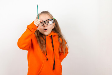 Wall Mural - A little girl in an orange suit, glasses and pencil. The concept of school, training, self-development. On a white background.