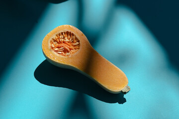 Overhead shot of a butternut squash that has been cut in half on blue turquoise background with shadows of tropical plants