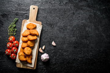 Poster - Chicken nuggets on a cutting Board with paper, cherry, garlic and thyme.