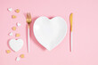 Valentine's Day background. Heart shaped white plate, knife and fork, scattered cute confetti hearts, gift with bow on isolated pastel pink background. Valentines day concept. Flat lay, top view, copy
