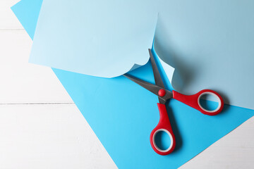 Canvas Print - Red scissors and light blue paper on white wooden background, top view